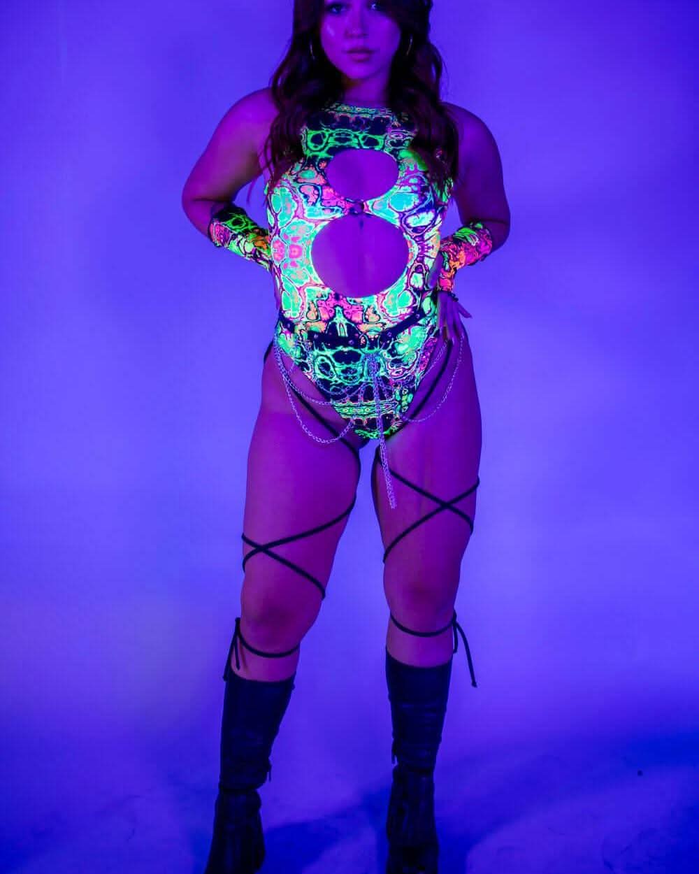 Model wearing Intensity Keyhole Bodysuit with leg straps, glowing under UV light, perfect for rave outfits.