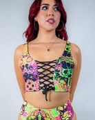 Model wearing the Intensity Lace Up Top, a UV reactive lace-up crop top with colorful skull design, perfect for rave outfits.