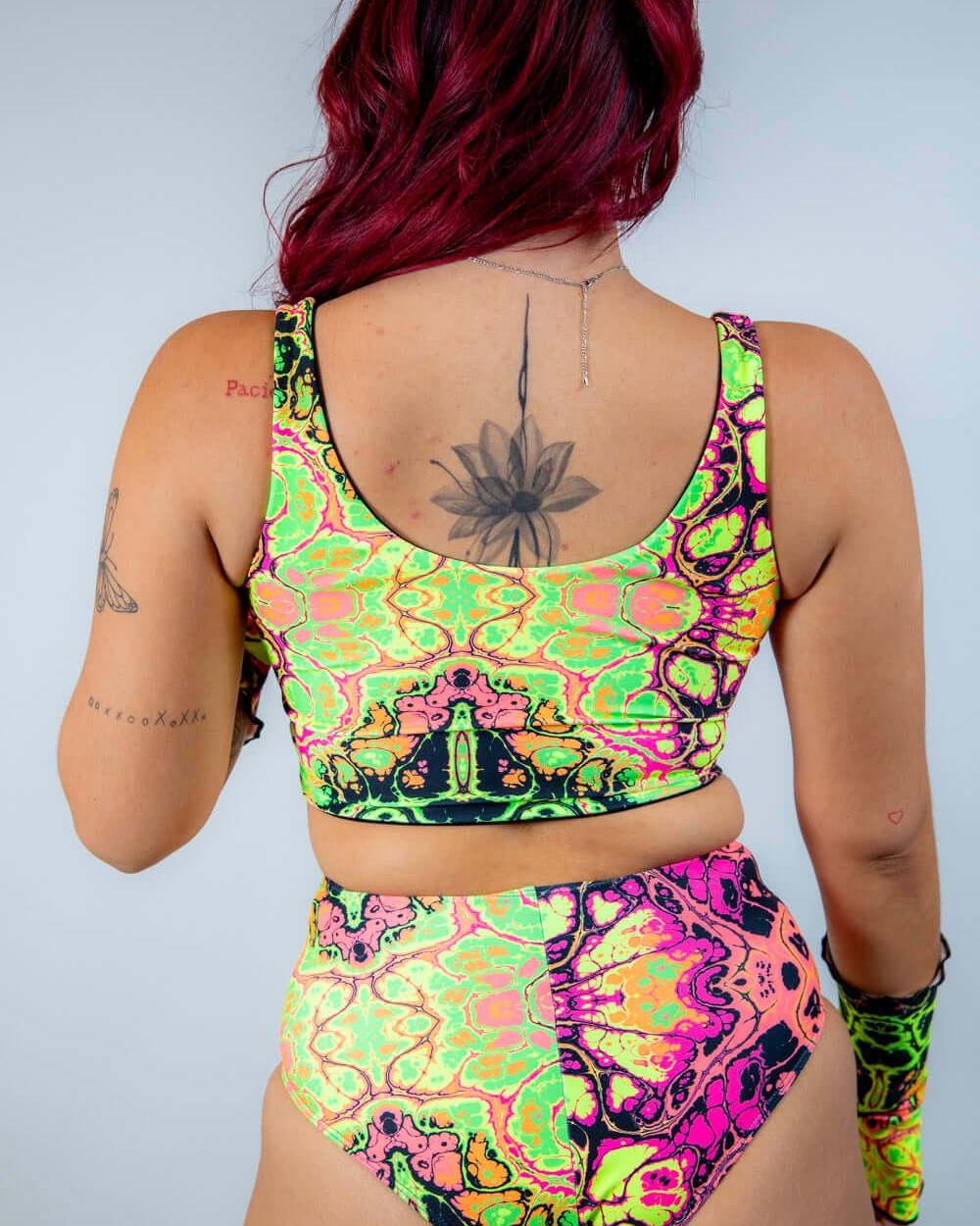 Back view of a model wearing a bright, UV reactive crop top and high-waisted bottom, perfect for rave outfits.