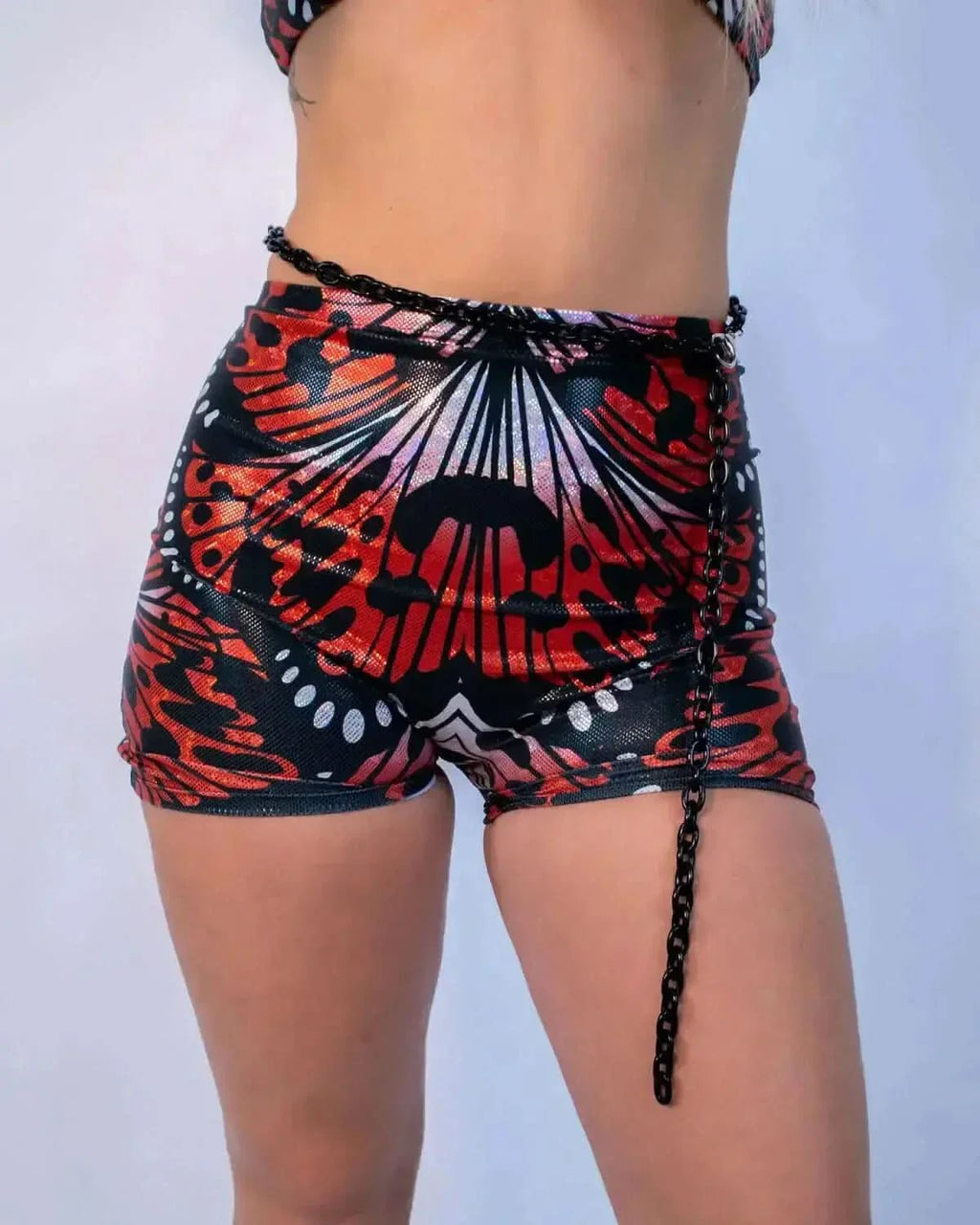 Red lacewing butterfly print rave pants with chain lacing details, festival outfit front view on model