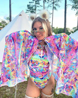 Woman in colorful rave outfit with mesh bell sleeves, standing outdoors at festival, exuding an ethereal vibe.