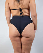 Back view of matte black high waisted rave pants style bikini bottoms showing cheeky coverage and festival outfit styling