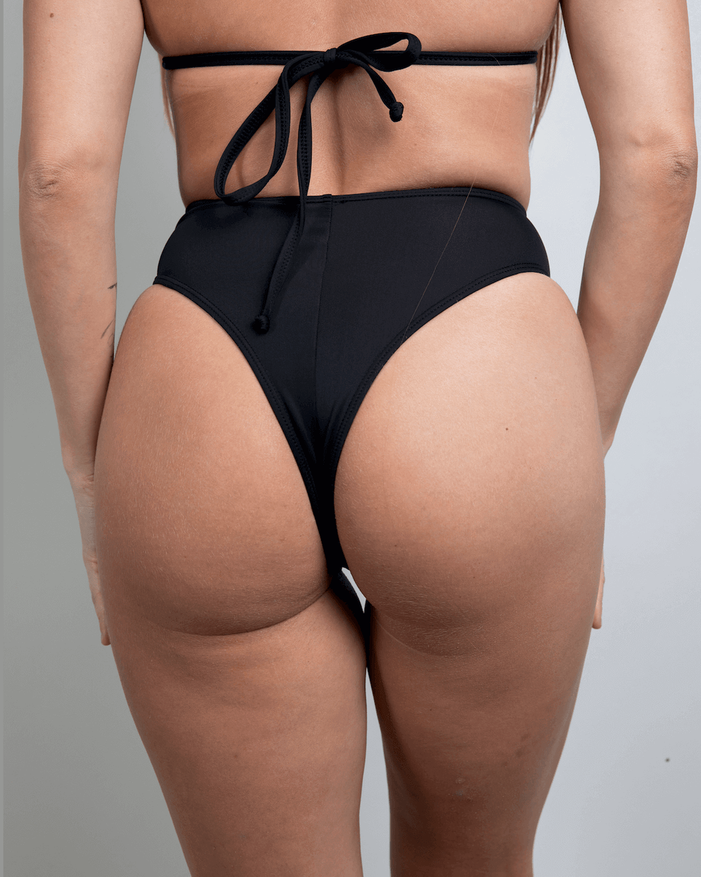 Matte black high waisted thong showcasing a cheeky cut, perfect for rave outfits and made from recycled materials.