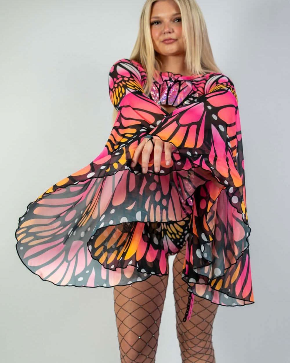 Blonde model wearing Monarch butterfly rave arm sleeves in pink orange gradient, arms extended showing flowing mesh
