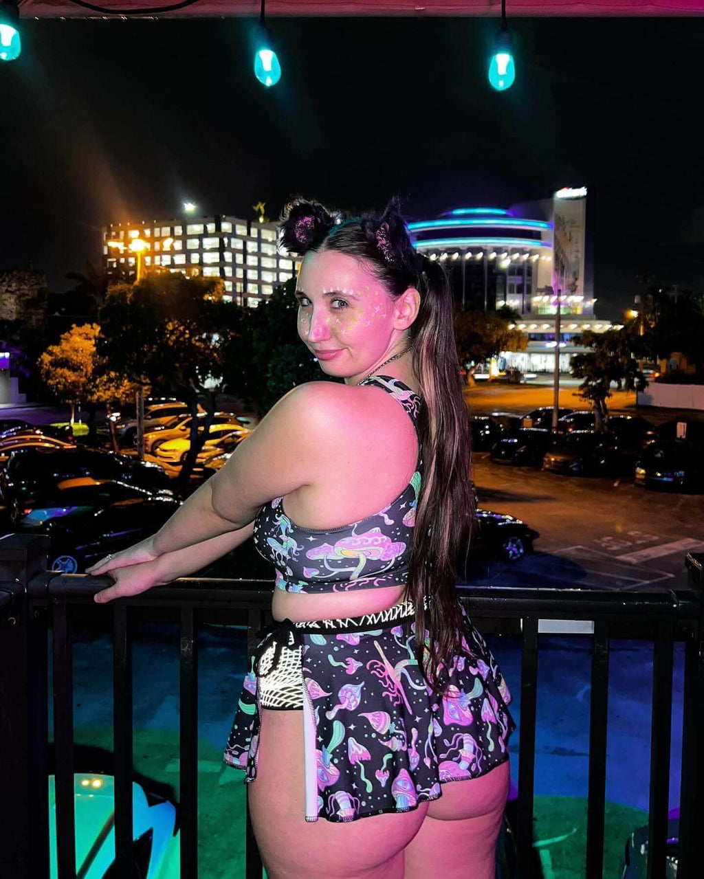 Woman in a magical outfit featuring a Mushies Swirl Skirt and crop top, posing at night with colorful lights in the background.
