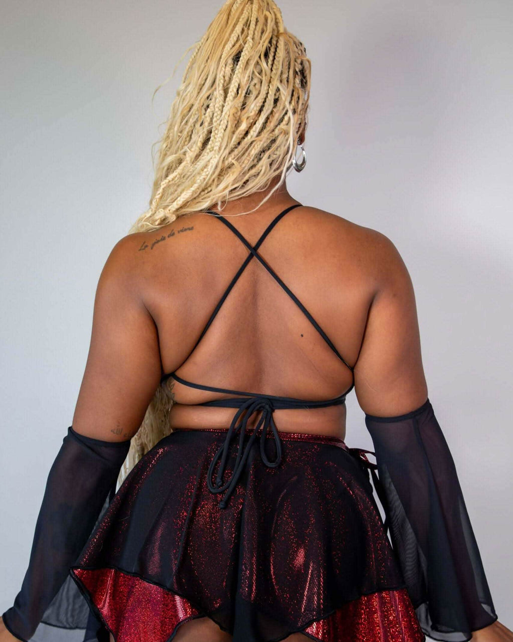 Back view of a model wearing the Phoenix Lush top with lace up design and a sparkly red skirt, suitable for rave outfits.