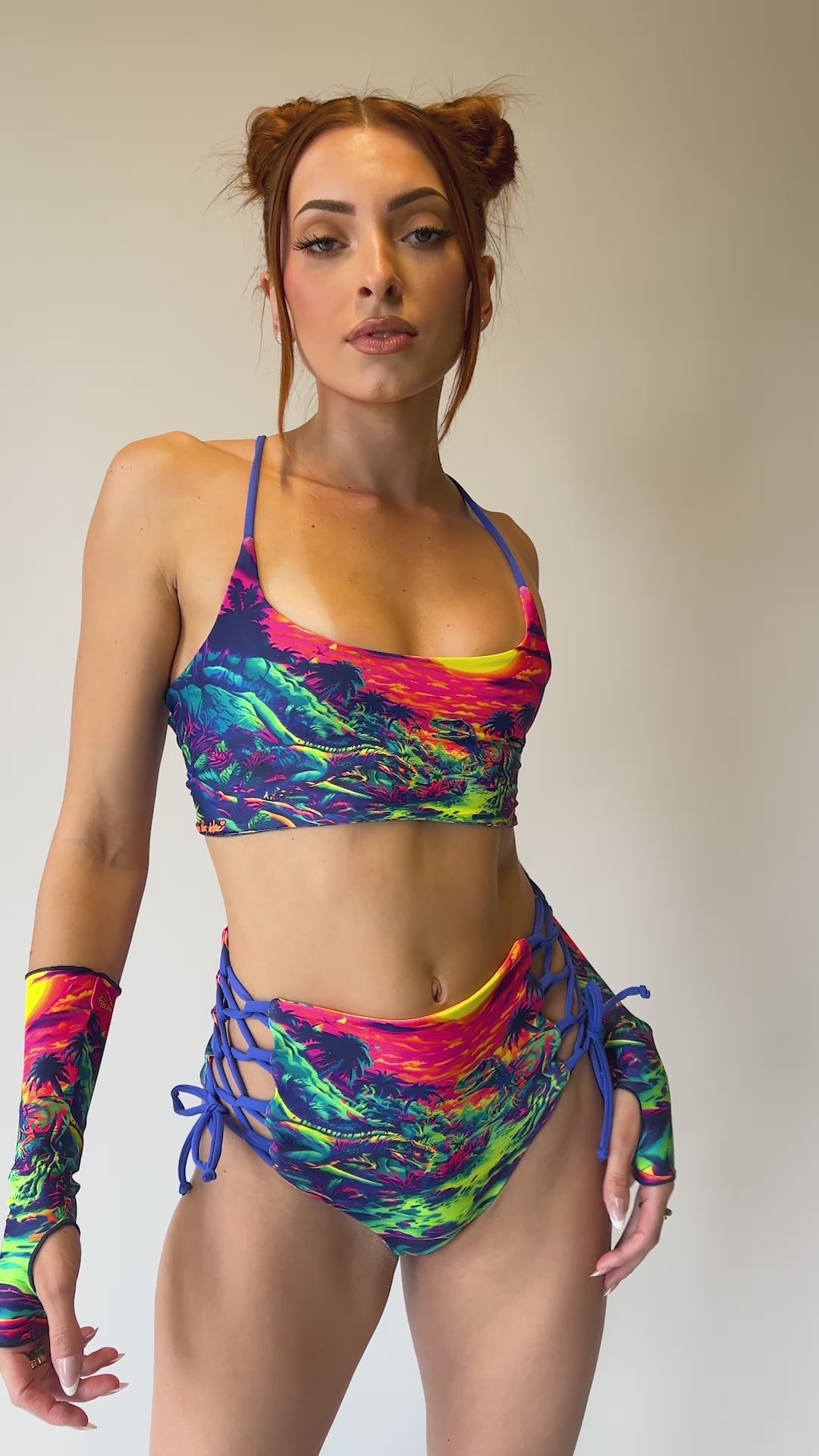 Model wearing Freedom Rave Wear vibrant two-piece set with neon dinosaur sunset print. Includes a bralette top and high-waisted lace-up shorts for rave style.