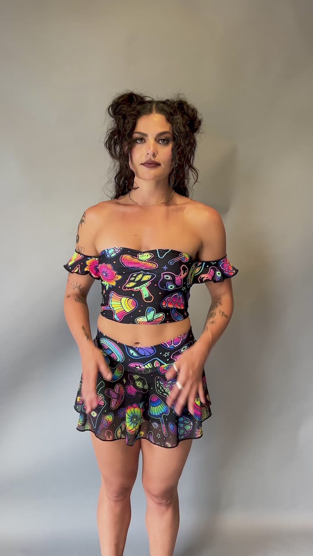 Model wearing a Freedom Rave Wear off-the-shoulder crop top with ruffle sleeves and matching high-waisted skirt in a psychedelic mushroom and flower print.