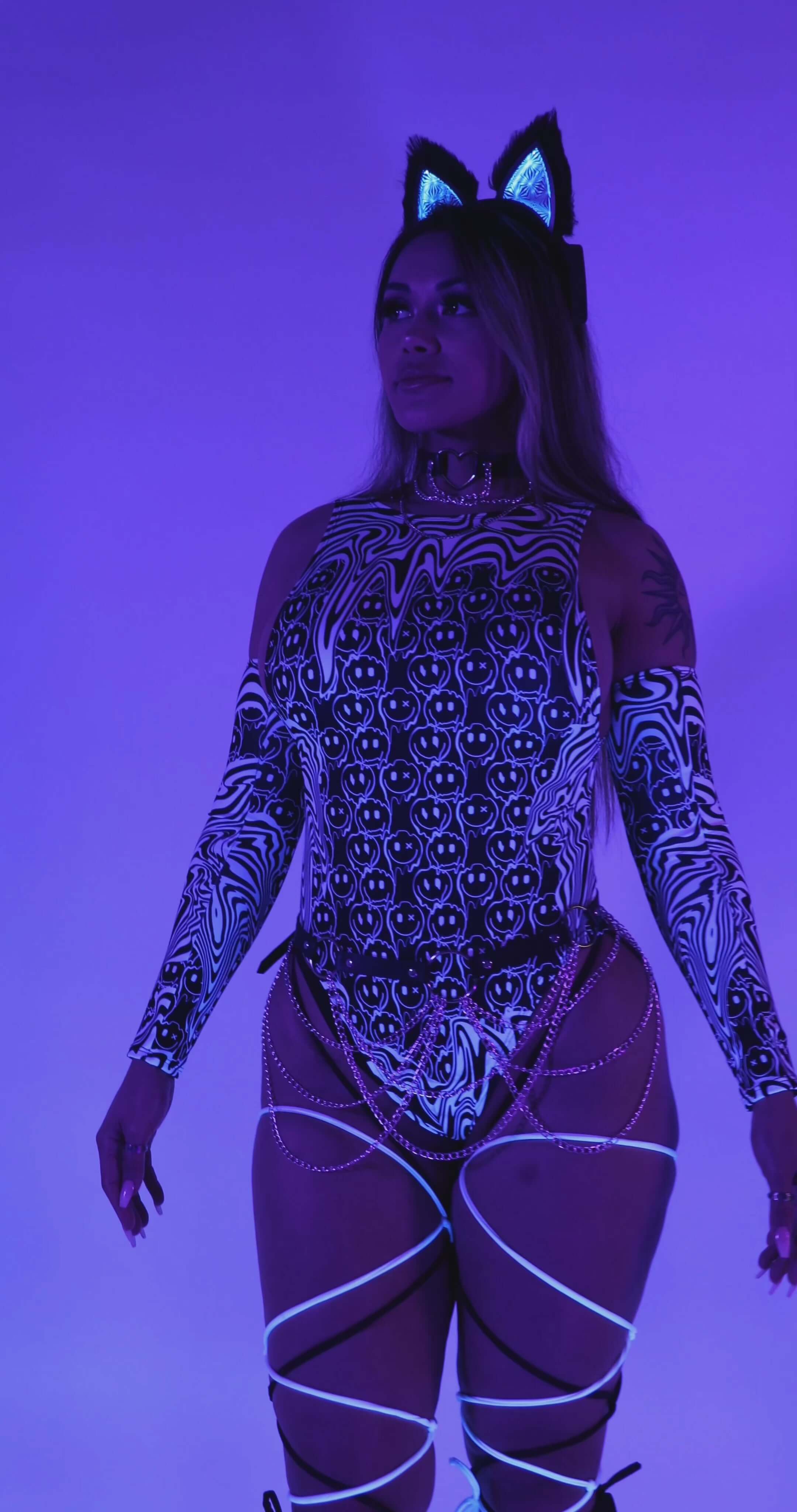 Model wearing the Meltdown Sideboob Bodysuit under blacklight, showing off its UV-reactive glow and trippy melty print.