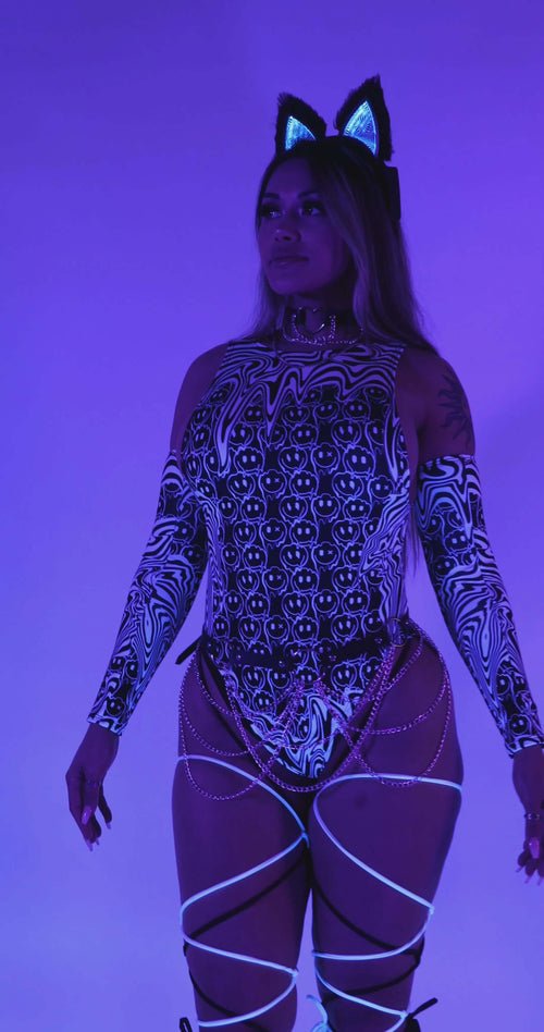 Model wearing the Meltdown Sideboob Bodysuit under blacklight, showing off its UV-reactive glow and trippy melty print.