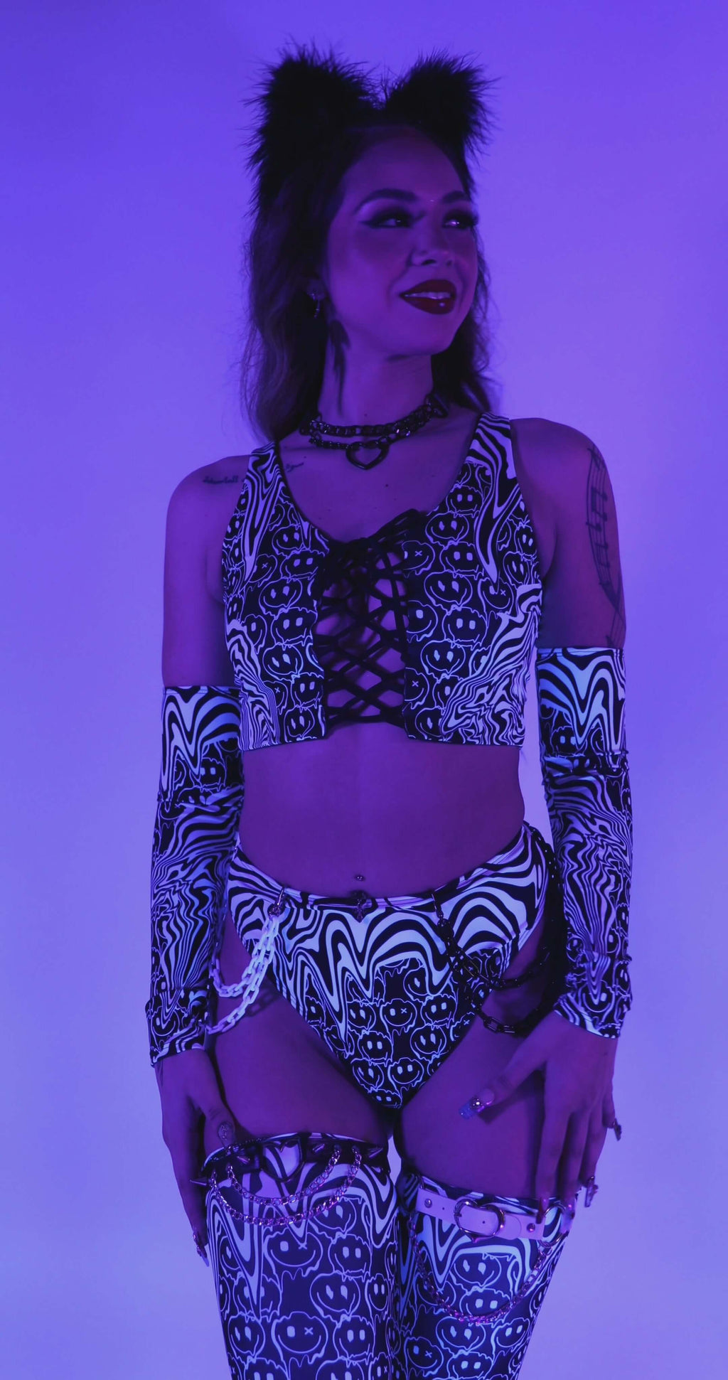 Model wearing the Meltdown Lace Up Top under blacklight, revealing its UV-reactive glow and bold trippy smiley print.
