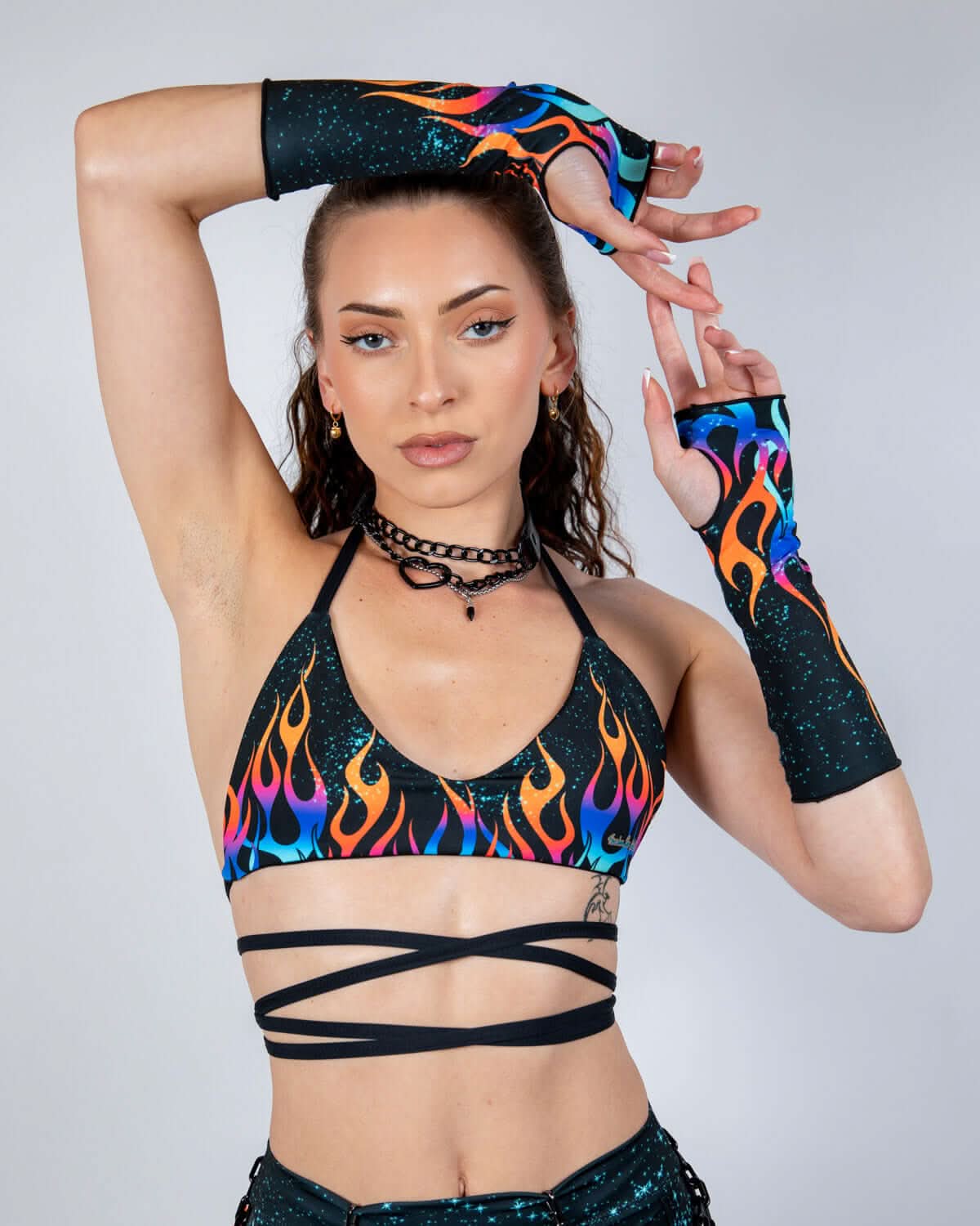 Model wearing Blaze rave arm sleeves with colorful flame pattern and holographic sparkles in dynamic festival pose