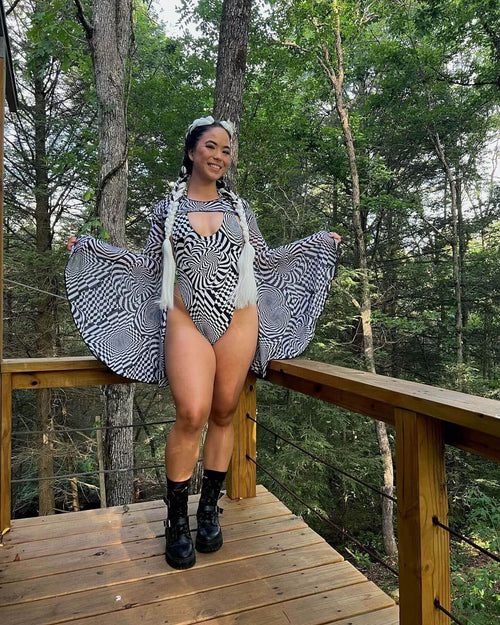 Woman modeling Distortion rave arm sleeves with optical print bodysuit on forest deck for festival outfit