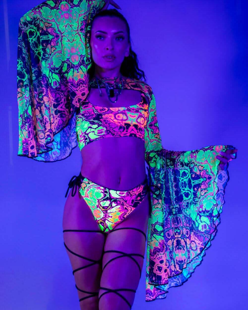 Model wearing Intensity mesh bell rave arm sleeves in neon psychedelic pattern under blacklight festival lighting