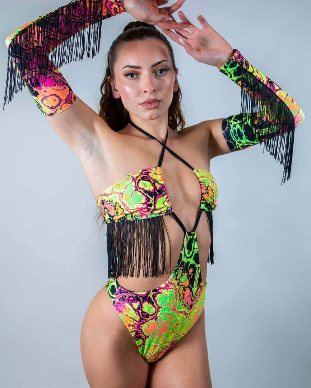 Model wearing Intensity rave arm sleeves with black fringe in neon psychedelic pattern, arms raised pose