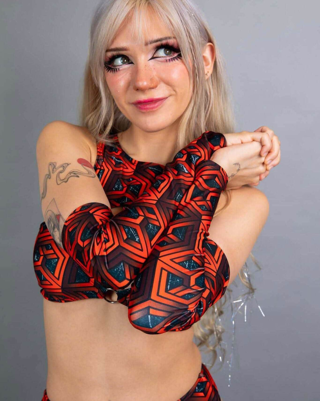 Model wearing red geometric Labyrinth rave arm sleeves in crossed arms pose for festival outfit styling