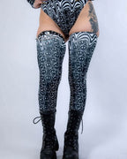 Black and white Meltdown rave arm sleeves with trippy smiley face pattern on model's legs for festival outfit