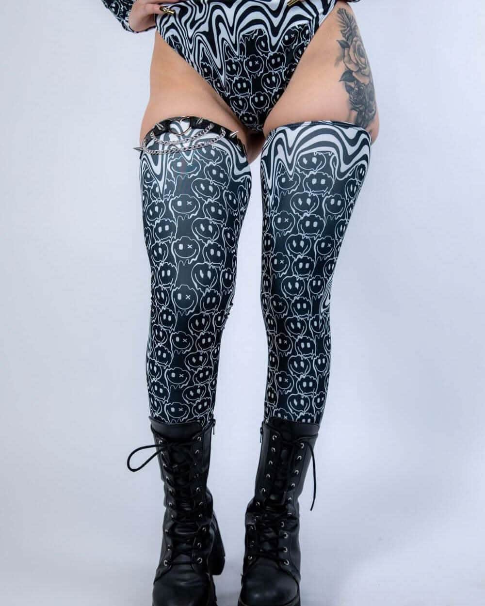 Black and white Meltdown rave arm sleeves with trippy smiley face pattern on model's legs for festival outfit