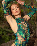 Model wearing Mesozoic tropical print rave arm sleeves with cutout details in forest setting for festival outfit styling