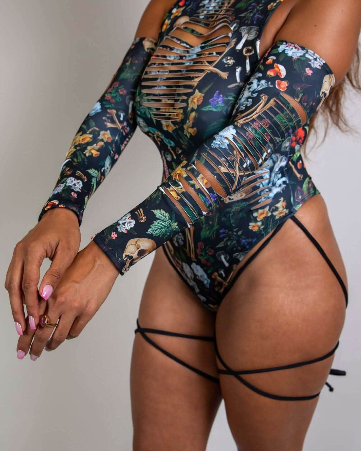 Poison rave arm sleeves with skull floral print shown on model from back angle with strappy bodysuit styling