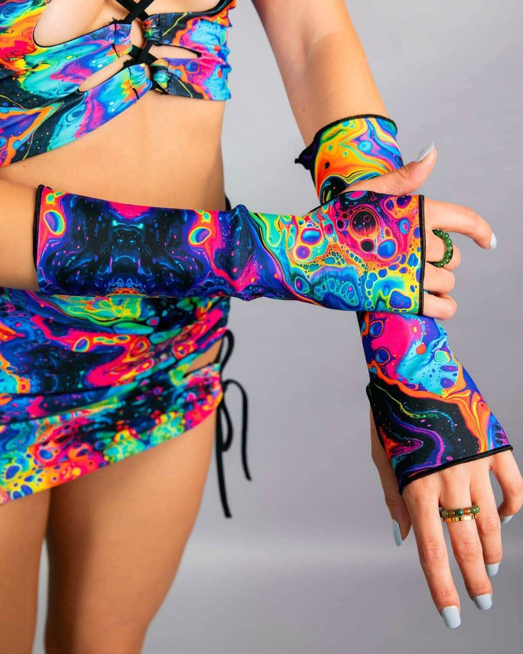 Model wearing vibrant psychedelic rave arm sleeves with rainbow swirl print in dynamic dance pose for festival outfit styling