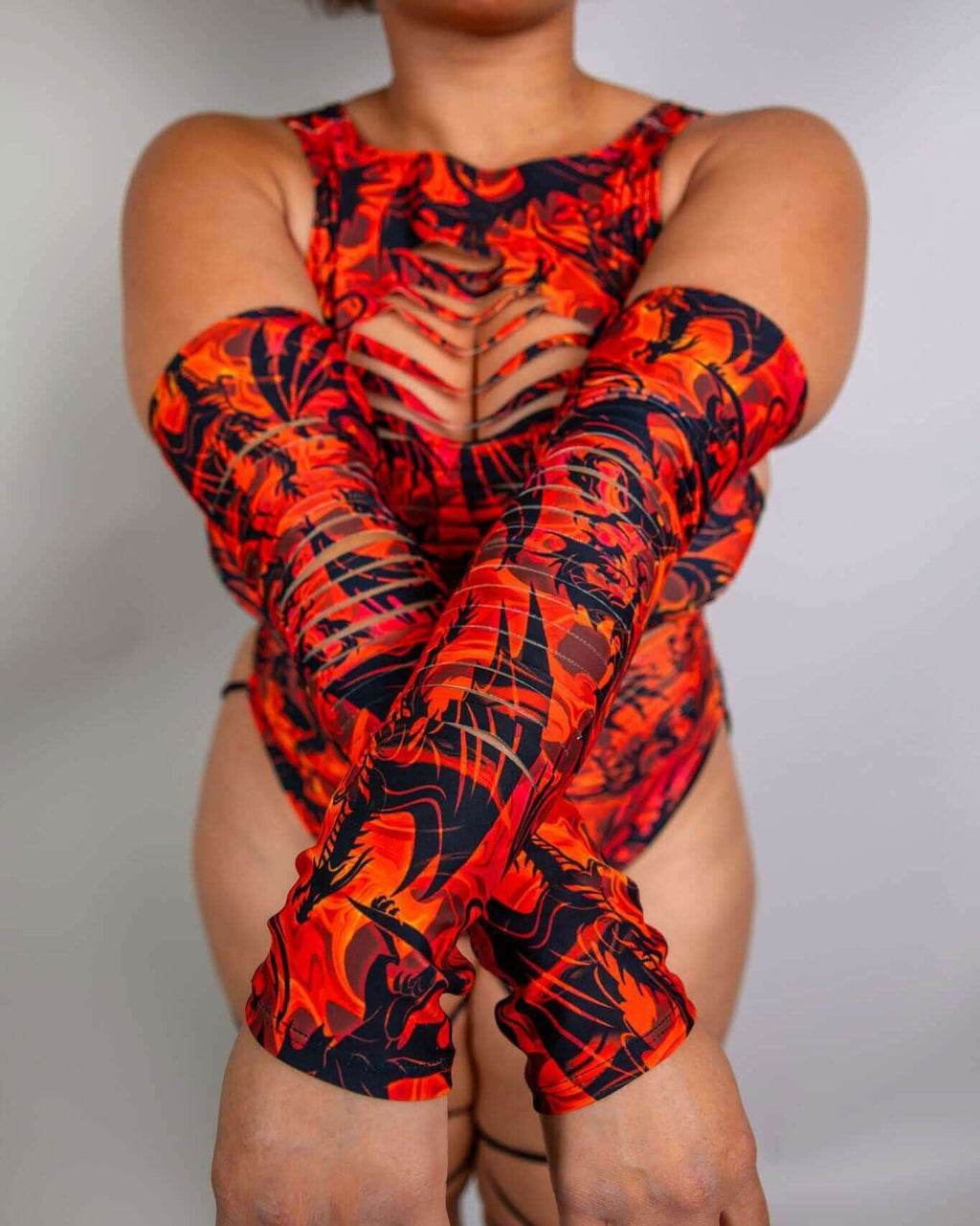Model wearing red dragon print rave arm sleeves with strategic slits, seated pose against white background