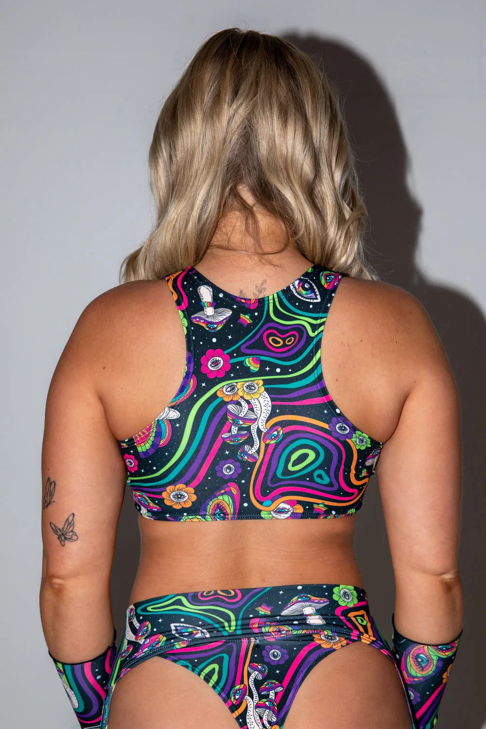 Awaken Keyhole Top, back view, featuring a vibrant psychedelic print with mushrooms, eyes, and neon swirling lines on a dark background. Freedom Rave Wear