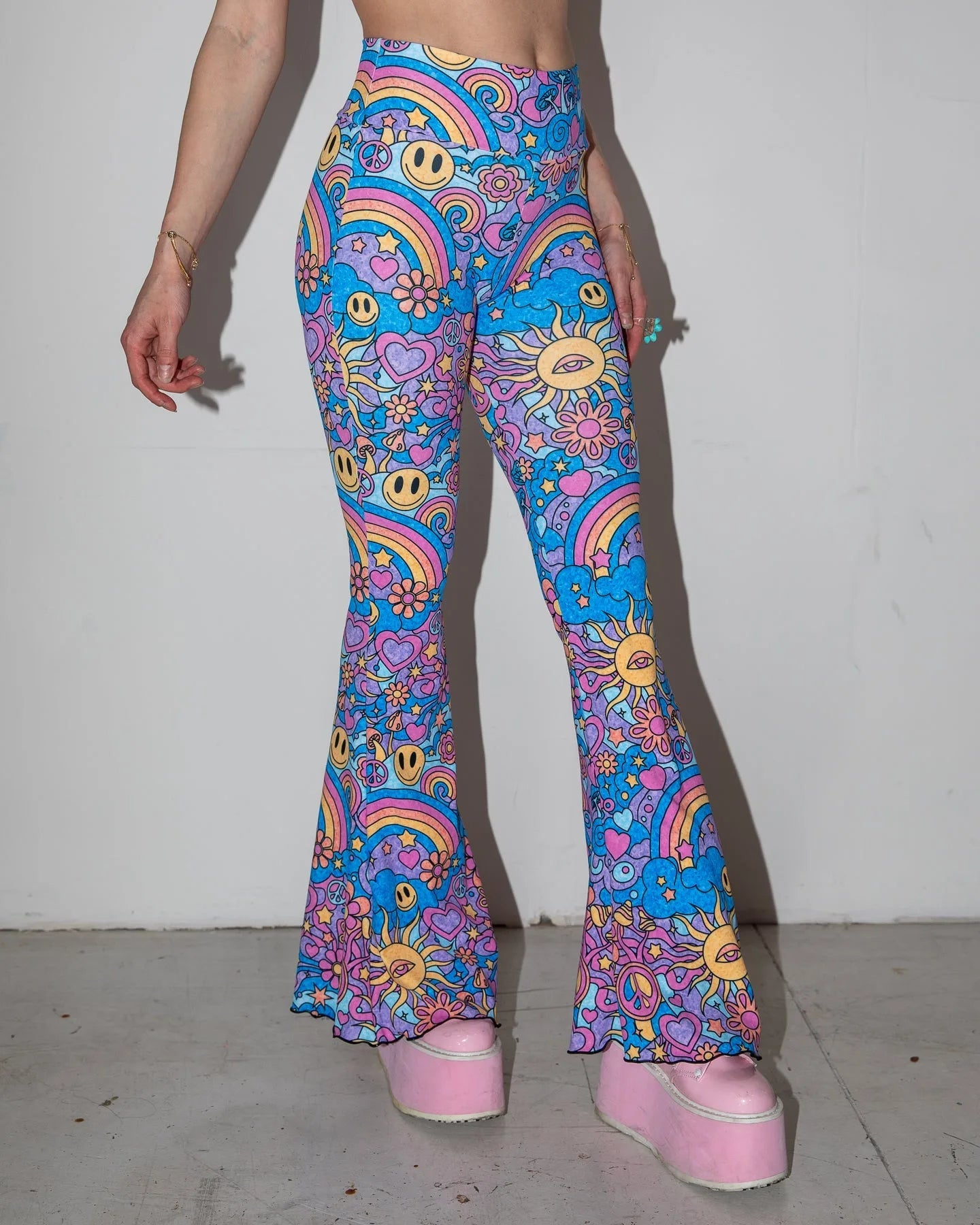 Groovy Bell Bottoms in a psychedelic blue and purple pattern, featuring smiley faces and rainbows, worn by a person facing front, ideal for festival fashion.