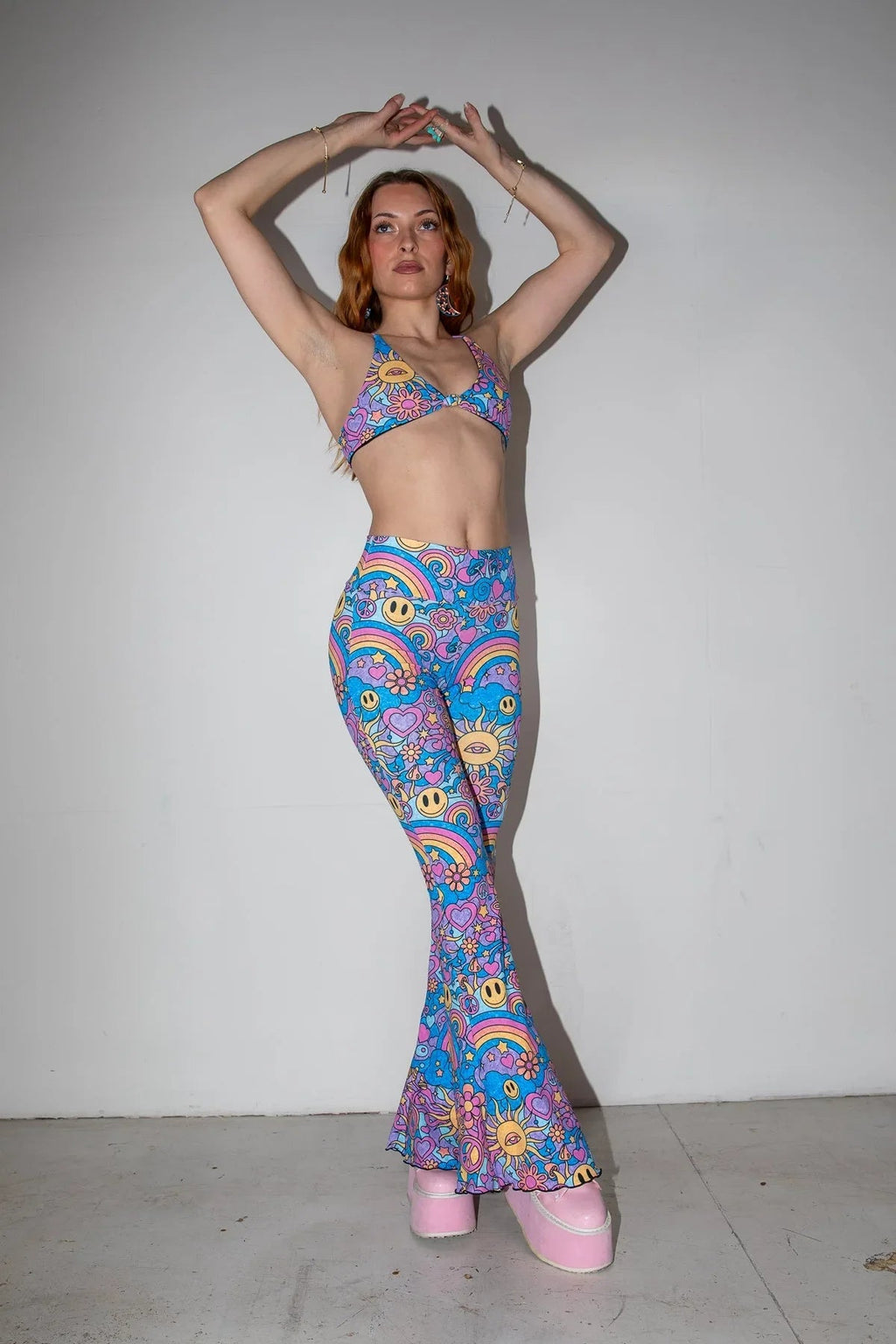 Front view of Groovy Bell Bottoms and matching top on a model, showcasing the psychedelic rave pattern with smiley faces and rainbows.