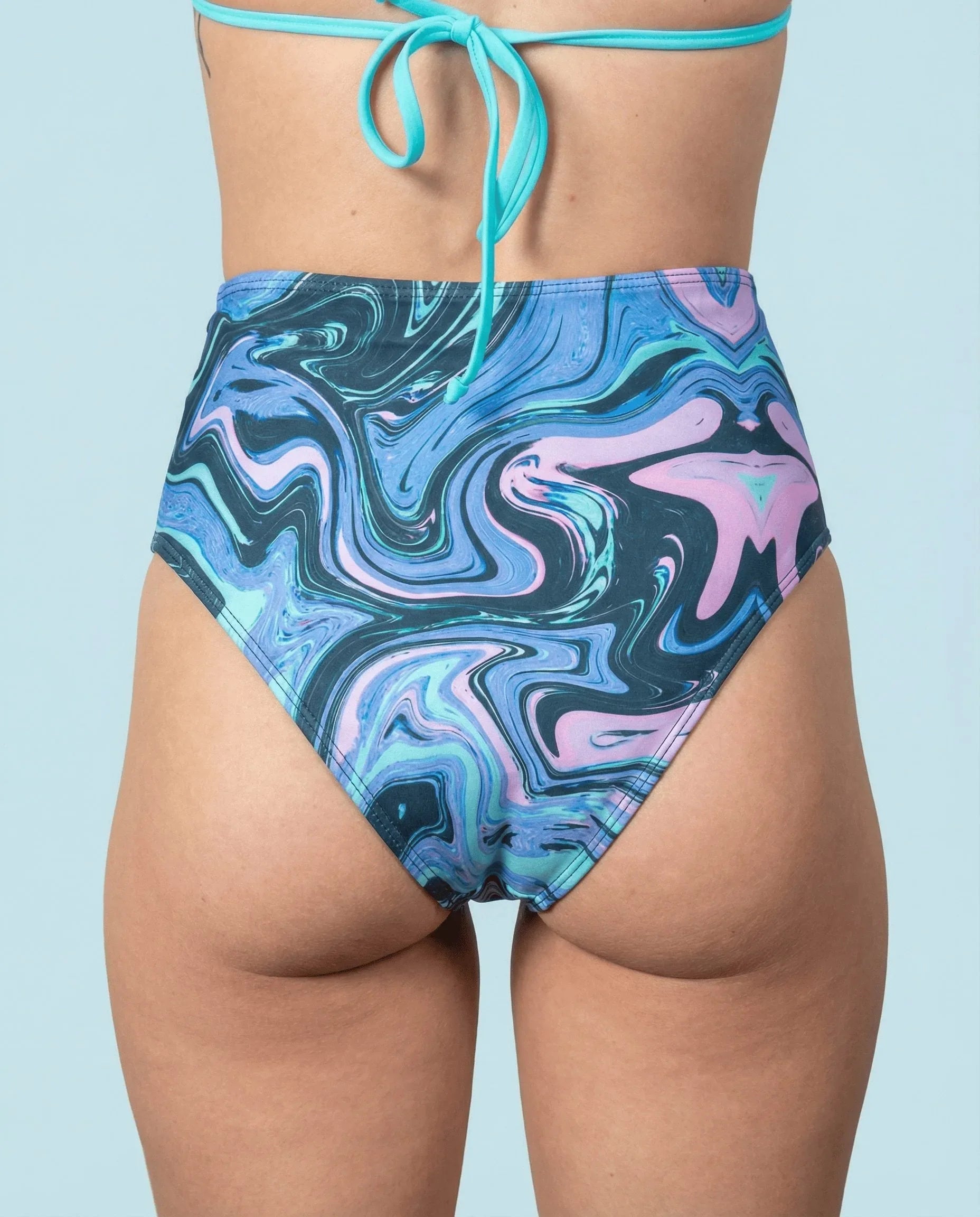 Glacial High Waisted Bikini Bottoms from the back, featuring a unique blue, teal, and lilac marbled rave pattern.