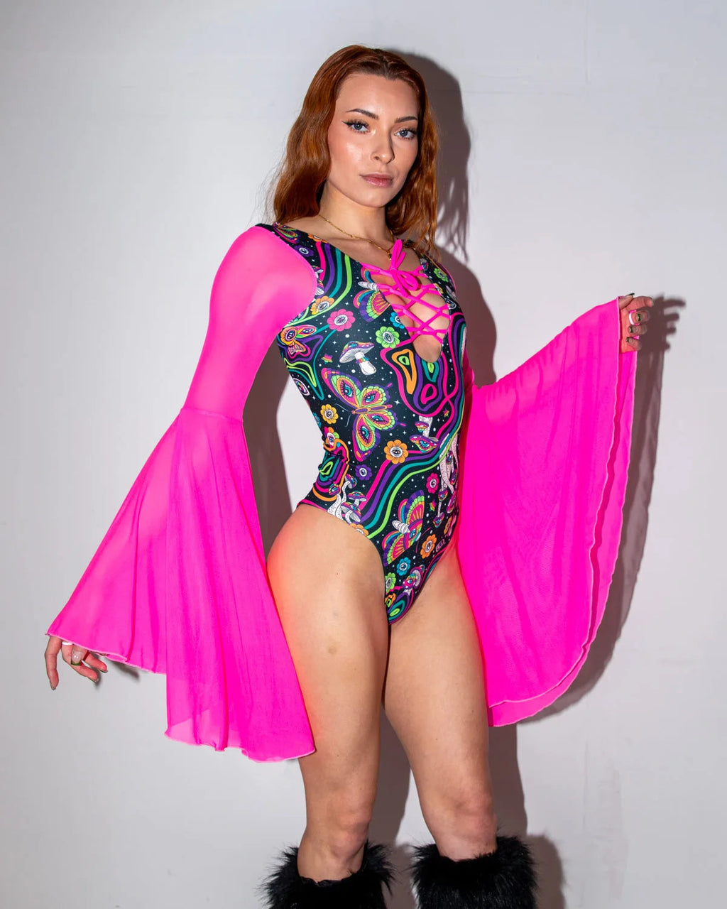 Awaken Goddess Bodysuit front view, featuring a model in a vibrant psychedelic pattern with neon pink sheer bell sleeves, perfect for rave festivals.