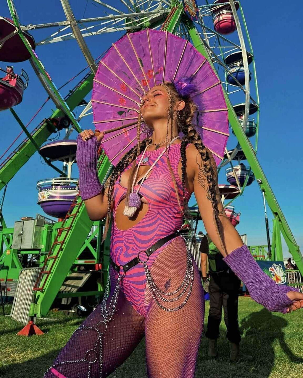 Woman wearing purple pink Cheshire rave bodysuit with parasol at festival carnival setting