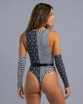 Confident woman in a black and white Duality rave bodysuit, showcasing unique geometric and optical stripe patterns from the back view.