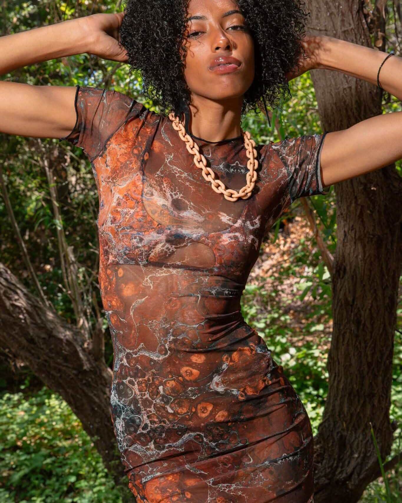 Woman wearing brown fossil print mesh maxi dress rave bodysuit styled outfit in natural outdoor setting