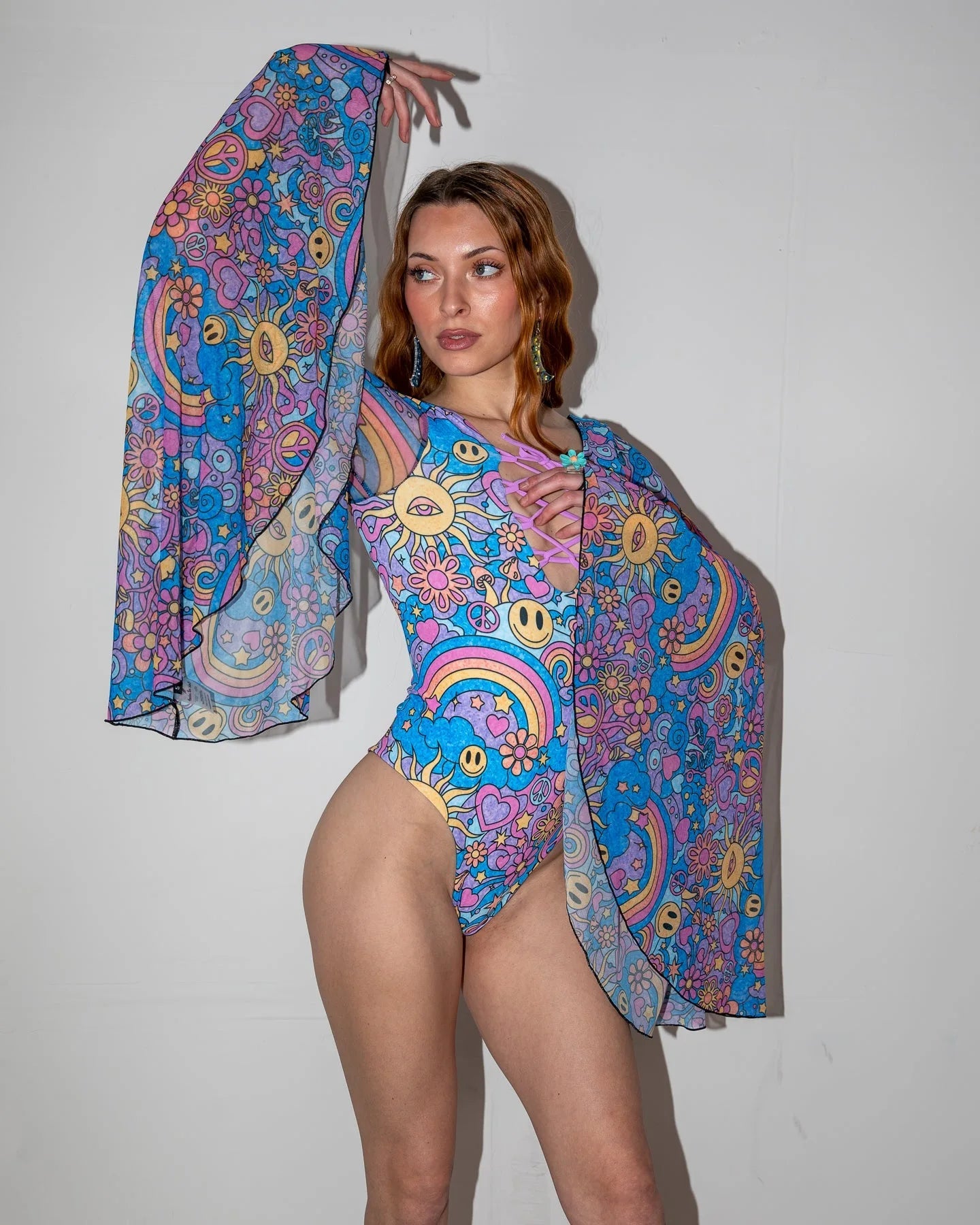 Groovy Goddess Bodysuit front view, featuring psychedelic smiley faces, peace signs, and suns in vibrant blue, pink, and yellow, perfect for a rave festival.
