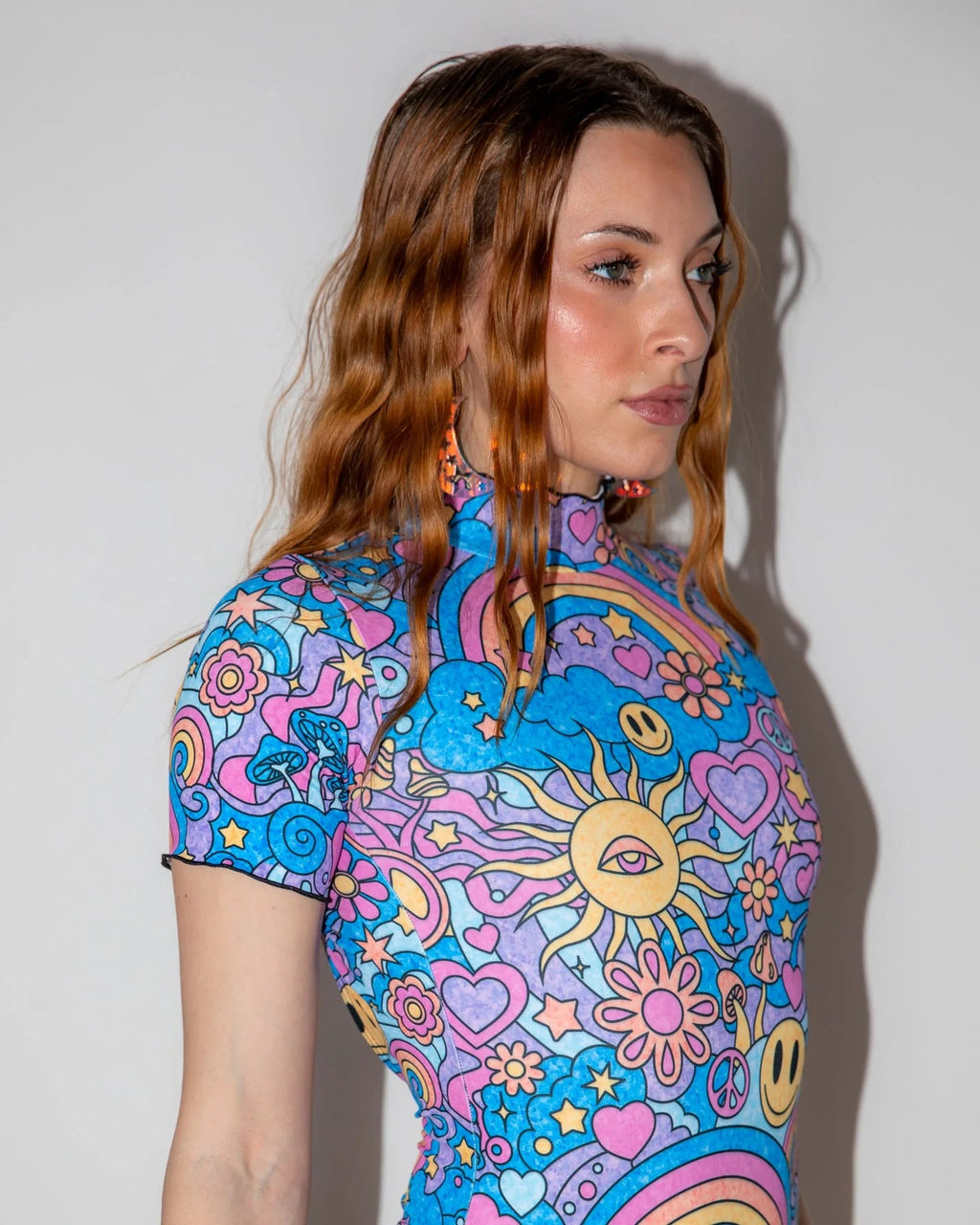 Groovy Wavy Baby Bodysuit from the side, showcasing the vibrant psychedelic pattern with smiley faces, mushrooms, and rainbows, perfect for a festival.