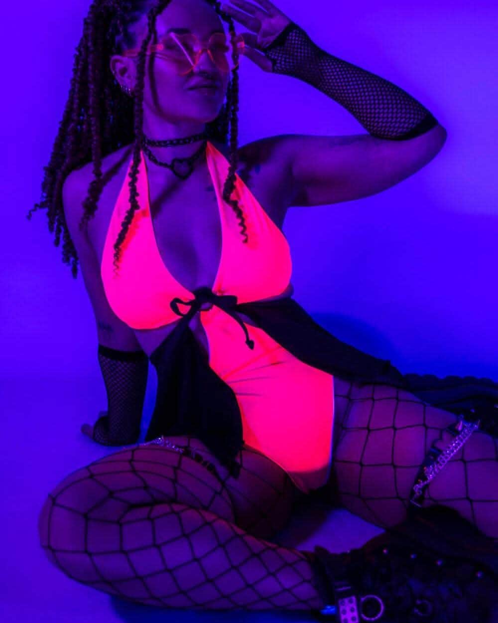 Hot pink rave bodysuit with black O-ring details and fishnet sleeves under UV festival lighting