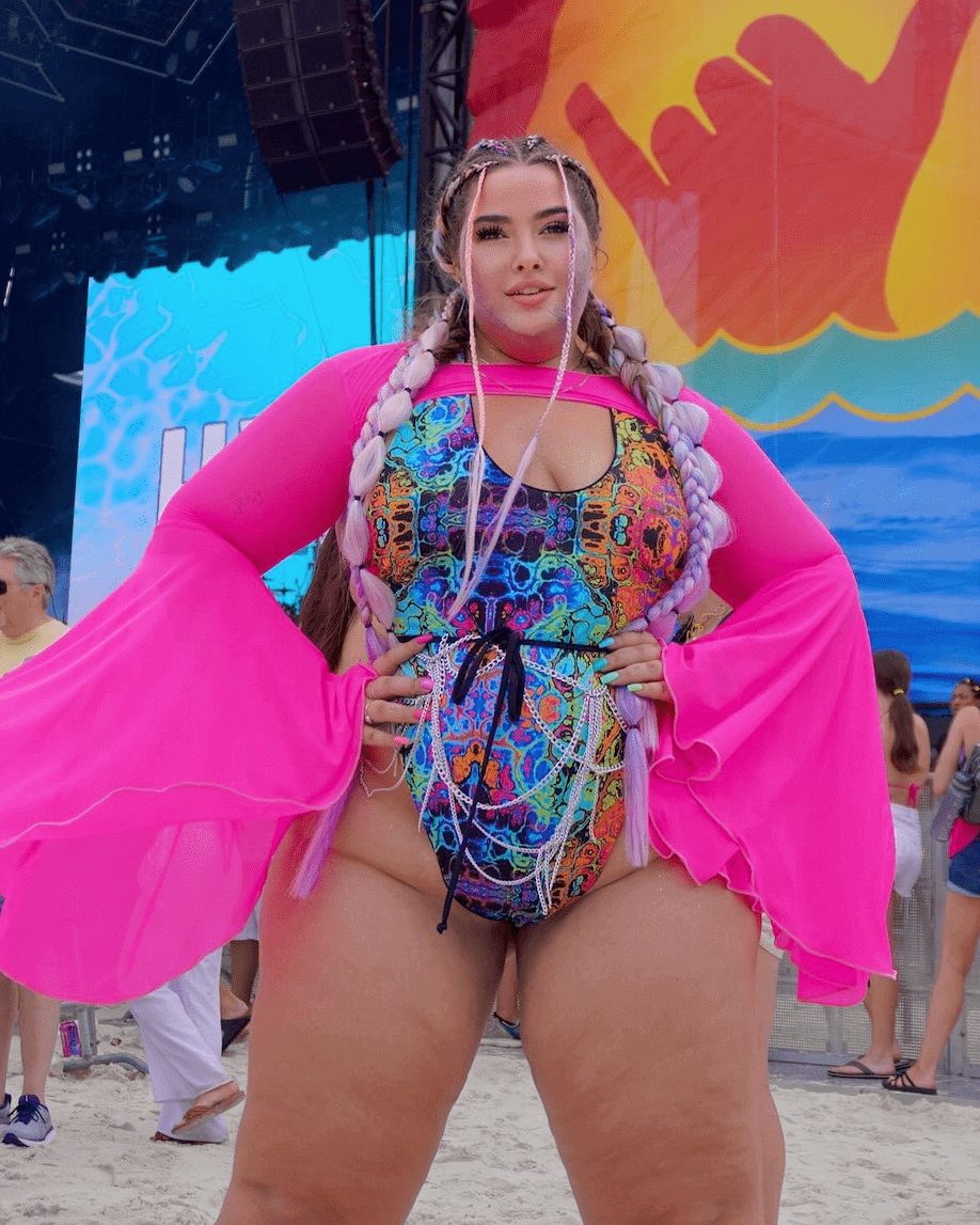 Woman wearing Lucidity Temptation rave bodysuit with pink cape at beach festival event