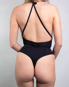 Back view of matte black rave bodysuit with crossed halter straps and open back design on model