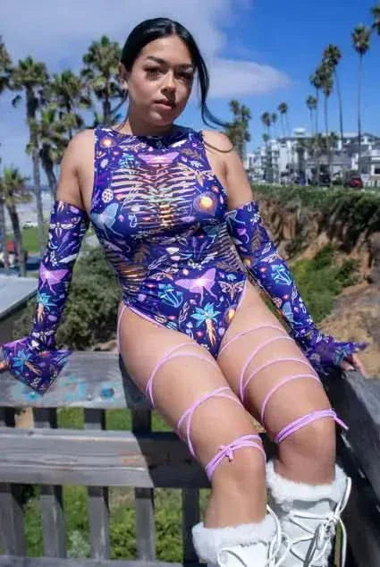 Model wearing purple galaxy Lucent rave bodysuit with side cutouts and pink leg straps outdoors