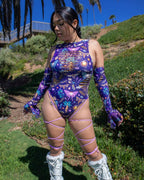 Purple Lucent rave bodysuit with sideboob cutouts and leg straps styled for festival outdoor photoshoot