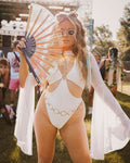 Model in white eco-luxe o-ring rave bodysuit with flowing cover-up holding holographic fan at festival