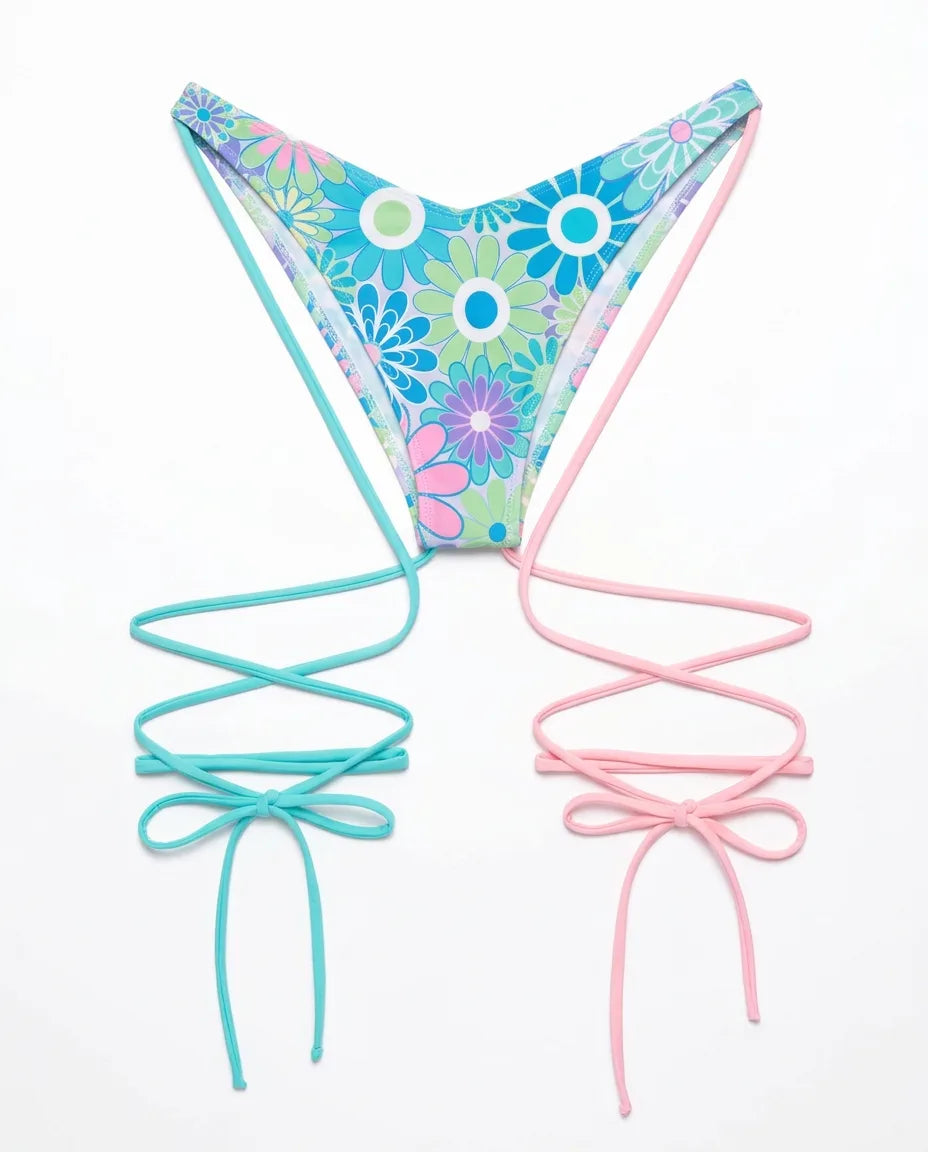 Flat lay of Retro Bloom Strappy High Hip Bottoms with vibrant floral print, featuring turquoise and pink tie details, perfect for festivals.