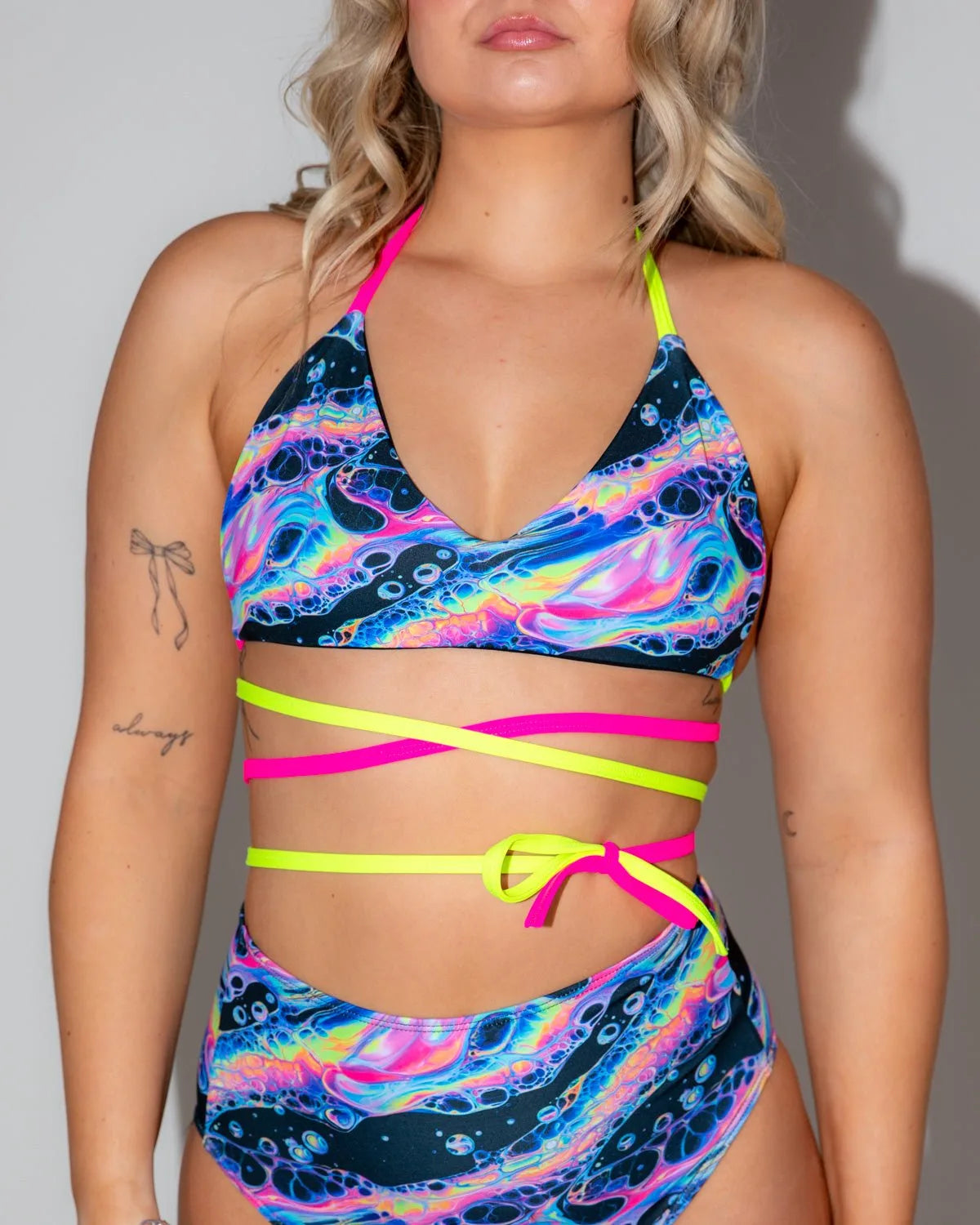 Acid Sky Extra Mile Bralette front view, featuring a psychedelic multi-color pattern and neon pink and yellow wrap straps, perfect for a rave festival.