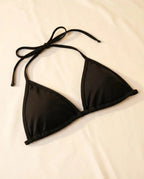 Close-up of a Women's Matte Black Bikini Top, a simple black triangle bikini top with tie straps, laid flat for festival wear.