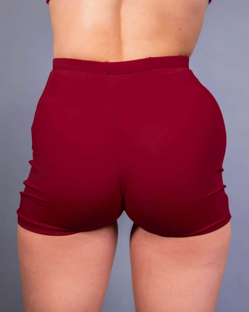 Back view of burgundy rave pants high waist shorts on model against gray background