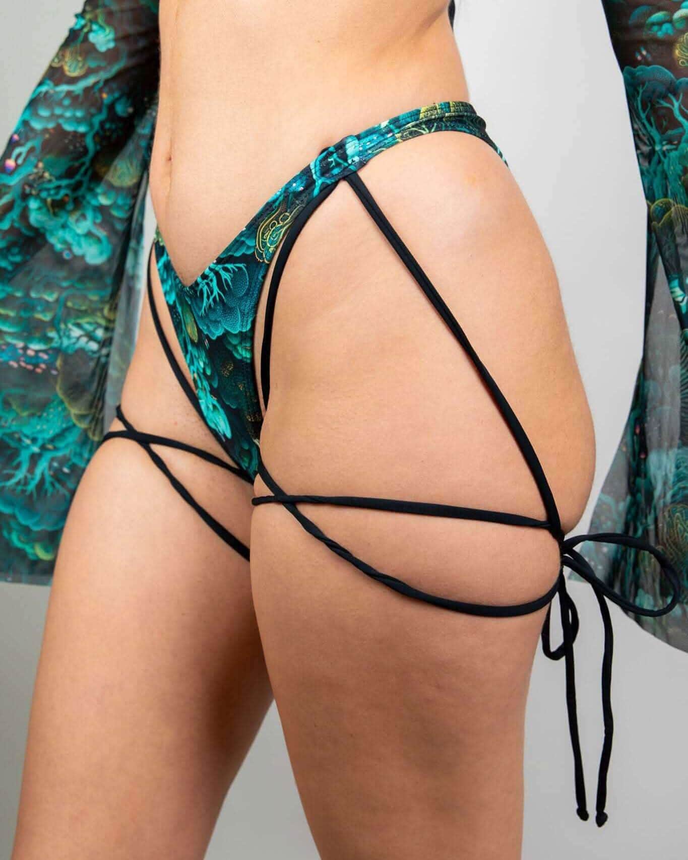 Faewood rave pants bottoms back view showing intricate black strappy tie details and teal festival pattern