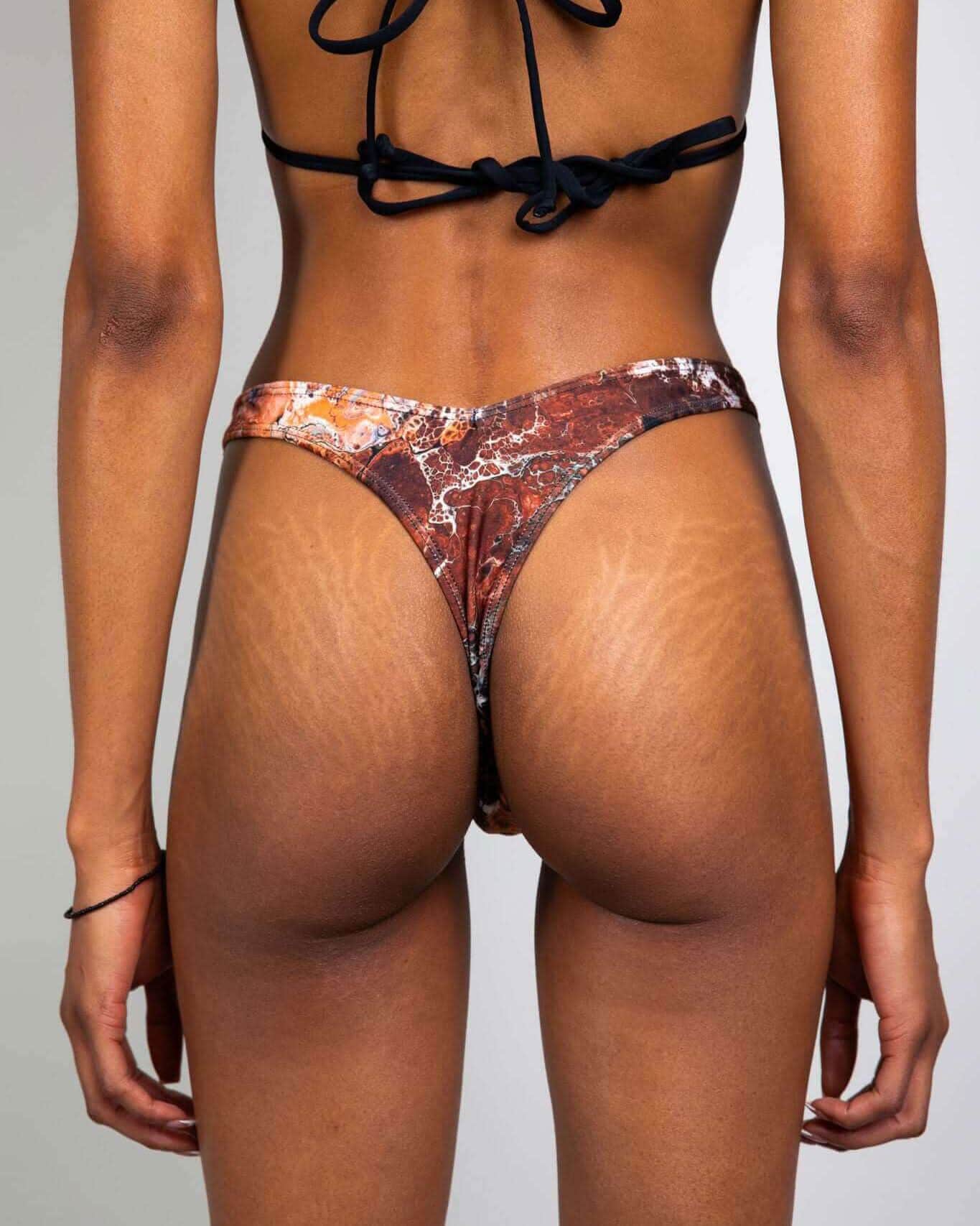 Back view of model wearing Fossil Risk rave pants with brown prehistoric pattern and black strappy top