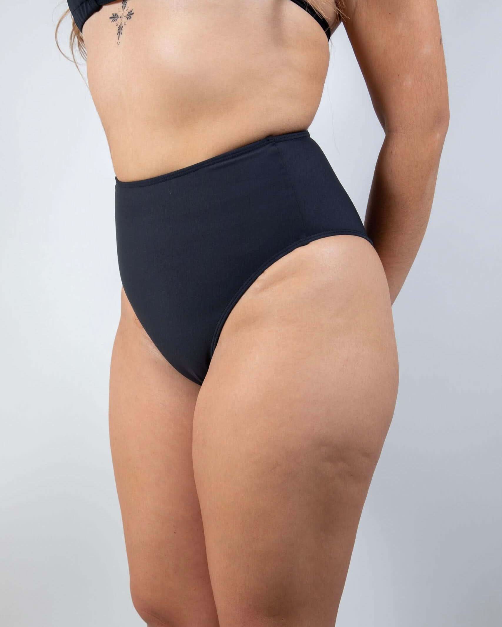 Matte black high waisted rave pants style bikini bottoms worn by model in side profile pose