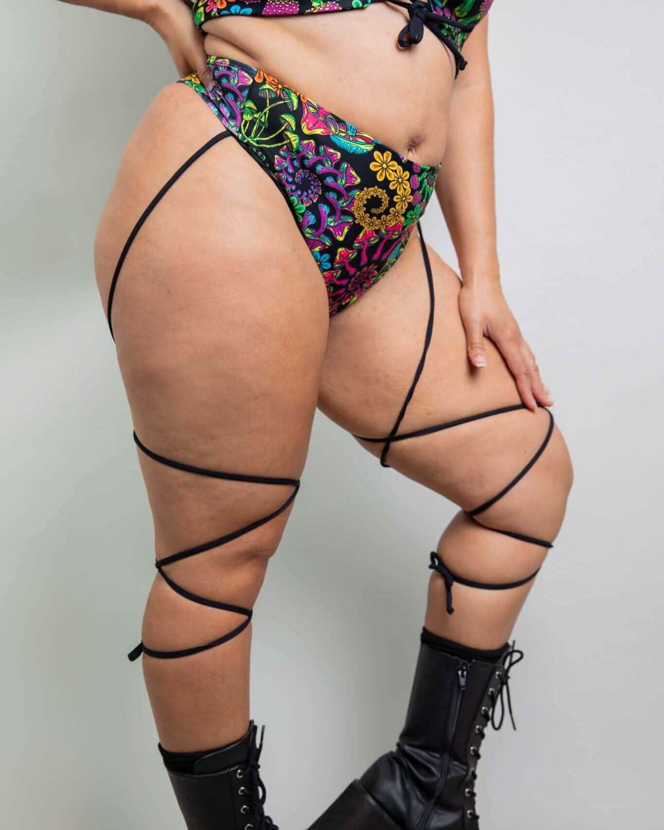 PsyBloom floral rave pants with black leg straps modeled from behind showing high-waisted thong festival outfit styling